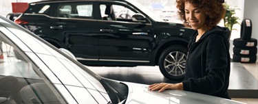 Woman admiring the appearance of her new car in a dealer’s showroom.