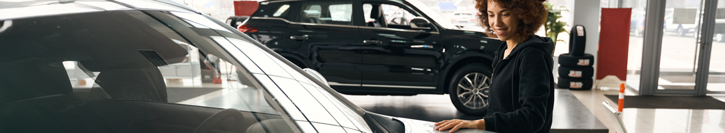Woman admiring the appearance of her new car in a dealer’s showroom.